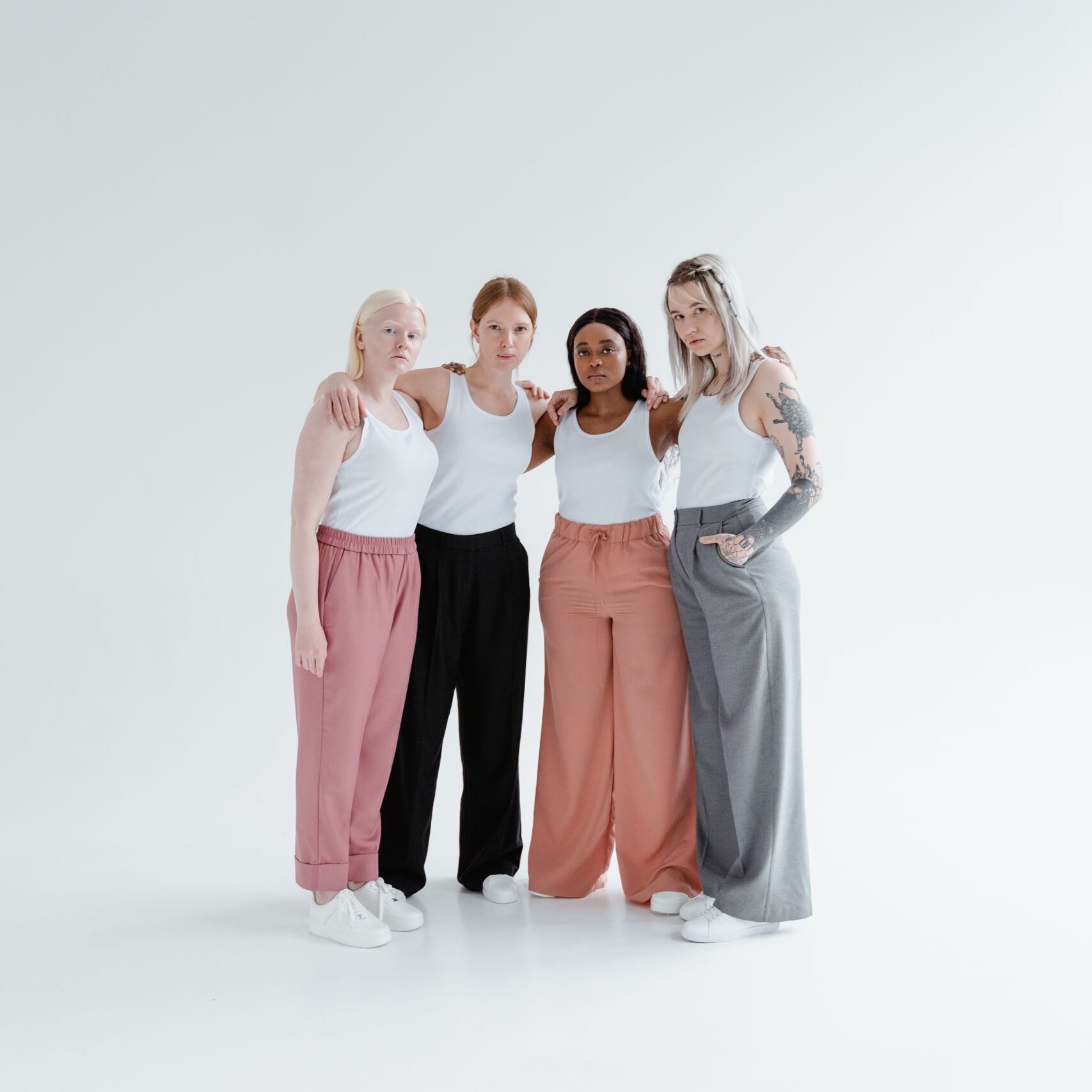 A group of diverse women wearing casual attire standing together in a studio embracing each other.