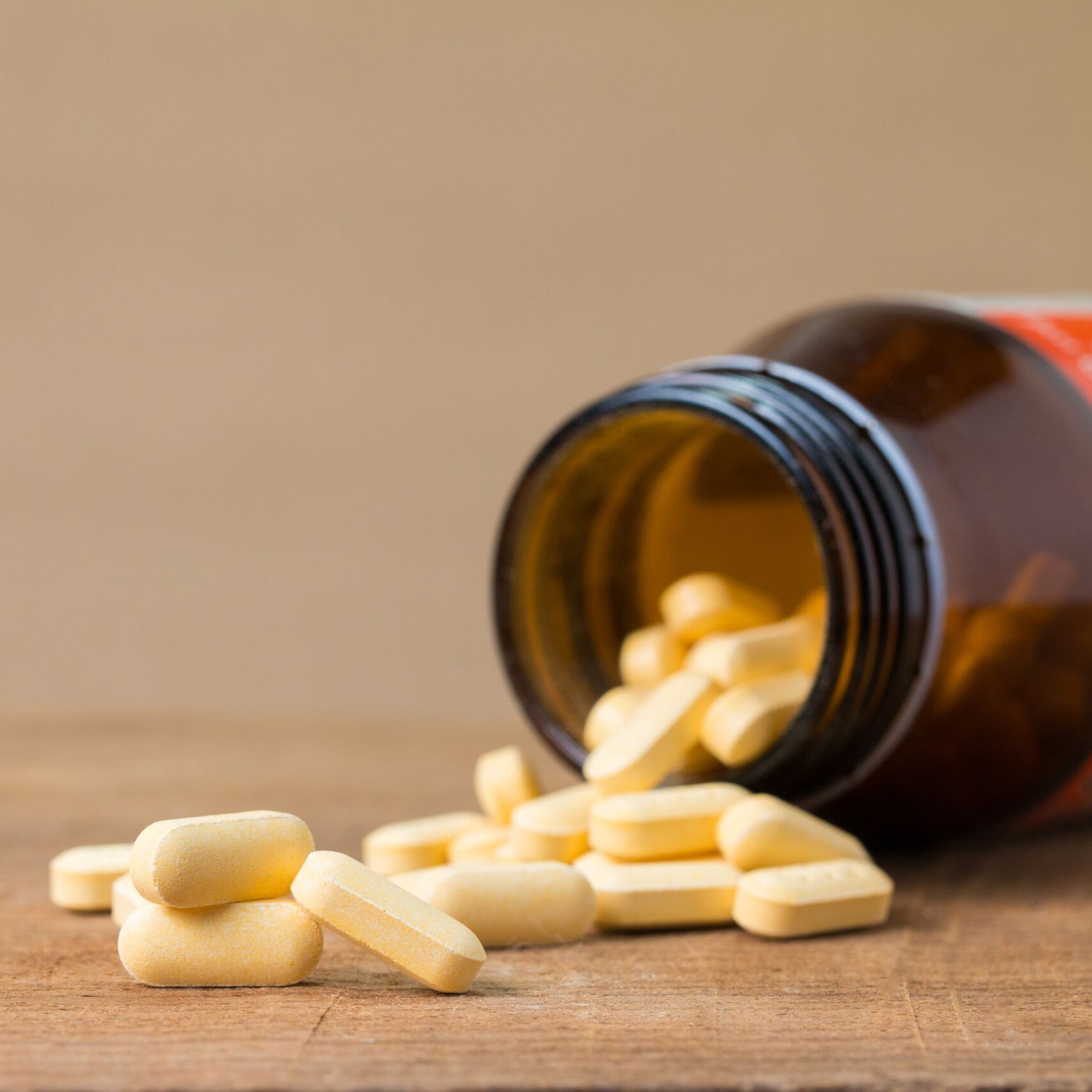 Yellow pills spill from a brown bottle onto a wooden surface, showcasing a health or medicine concept.