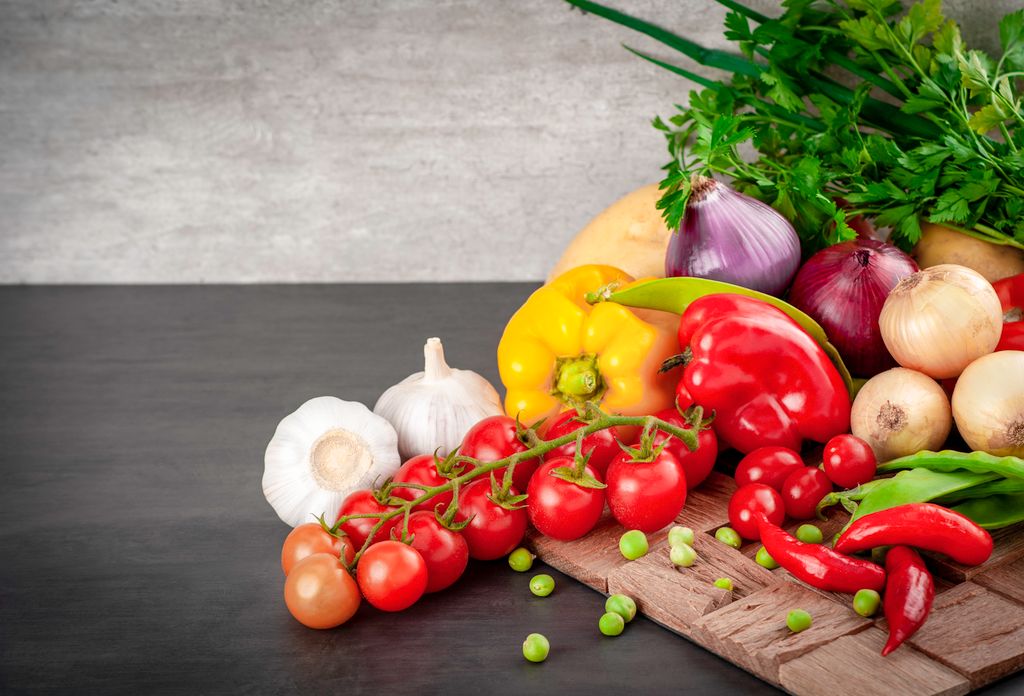 A vibrant selection of fresh vegetables including bell peppers and tomatoes on a wooden board.