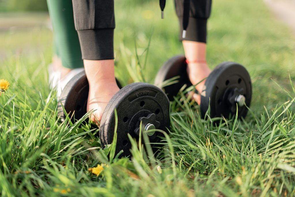 Close-up of a person exercising outdoors with dumbbells on grass, emphasizing fitness and wellness.