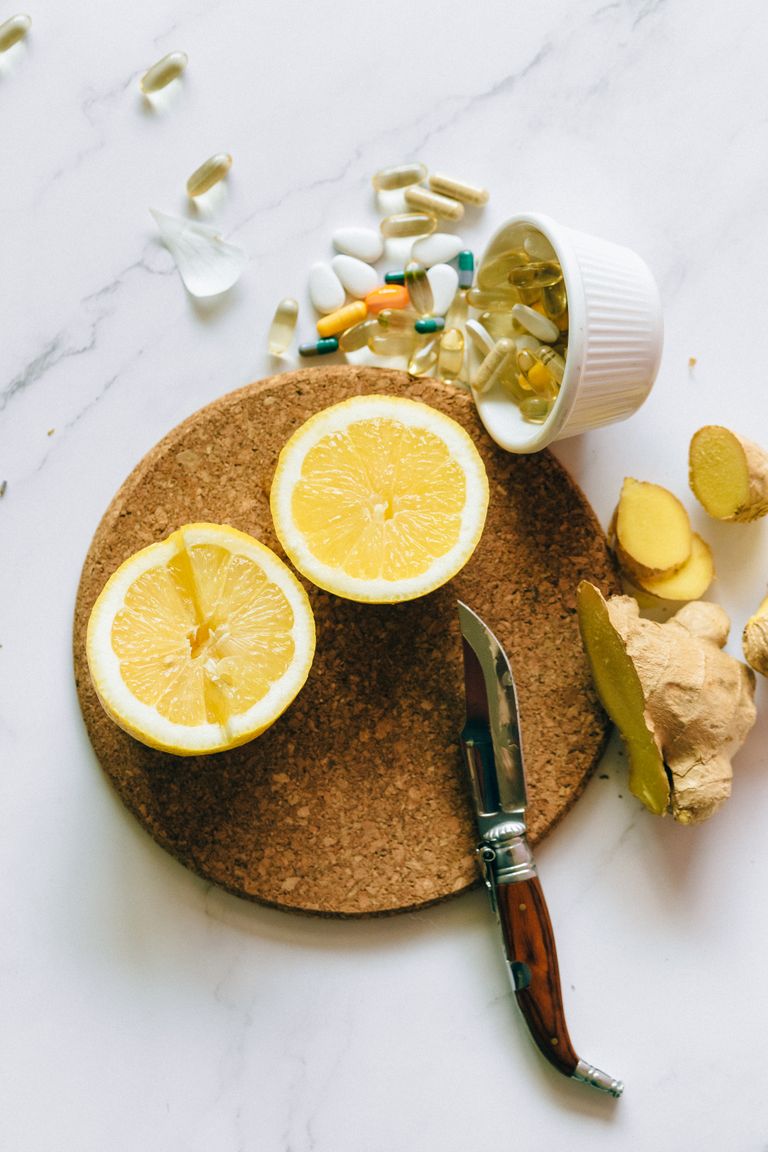 Flat lay of natural remedy ingredients including lemon, ginger, and supplements on a cork board.