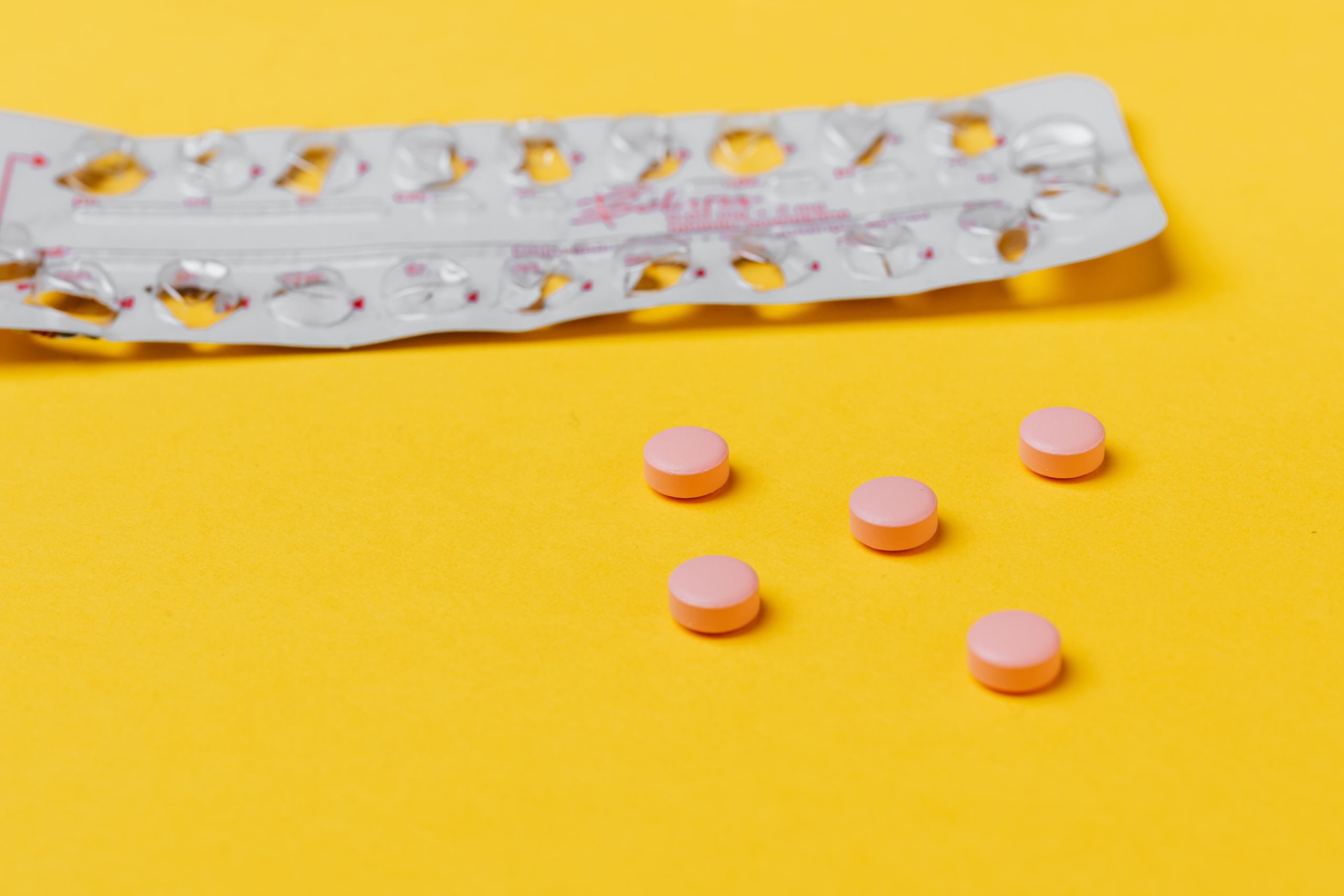 Pink pills and empty blister pack on a vibrant yellow surface.